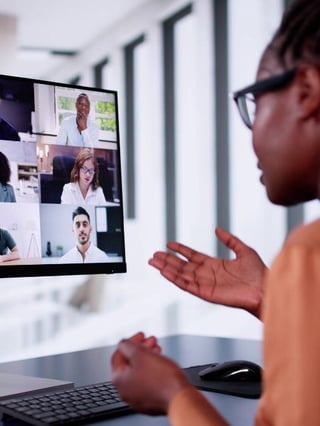 "Person participating in a webinar, with a computer screen showing a video call featuring multiple participants in a professional setting.