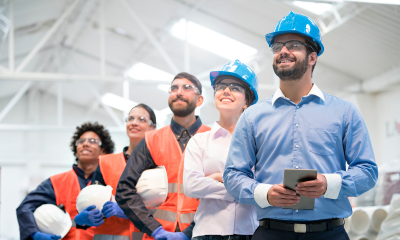 Image shows five workers holding hard hats and looking in to the distance