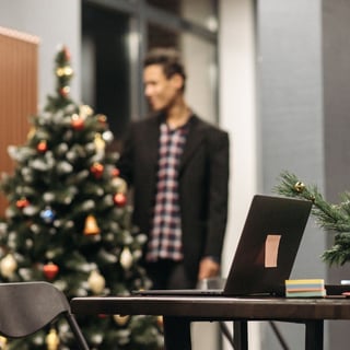 Image shows open laptop in the foreground, with a Christmas tree and person walking away in the background.